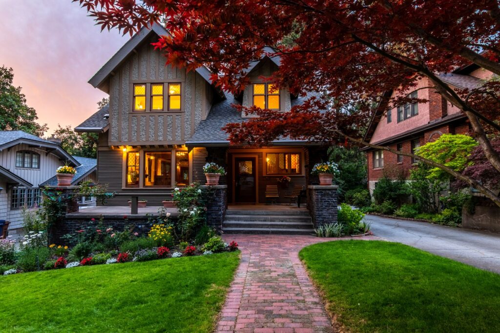 Warmly lit home with red maple at dusk